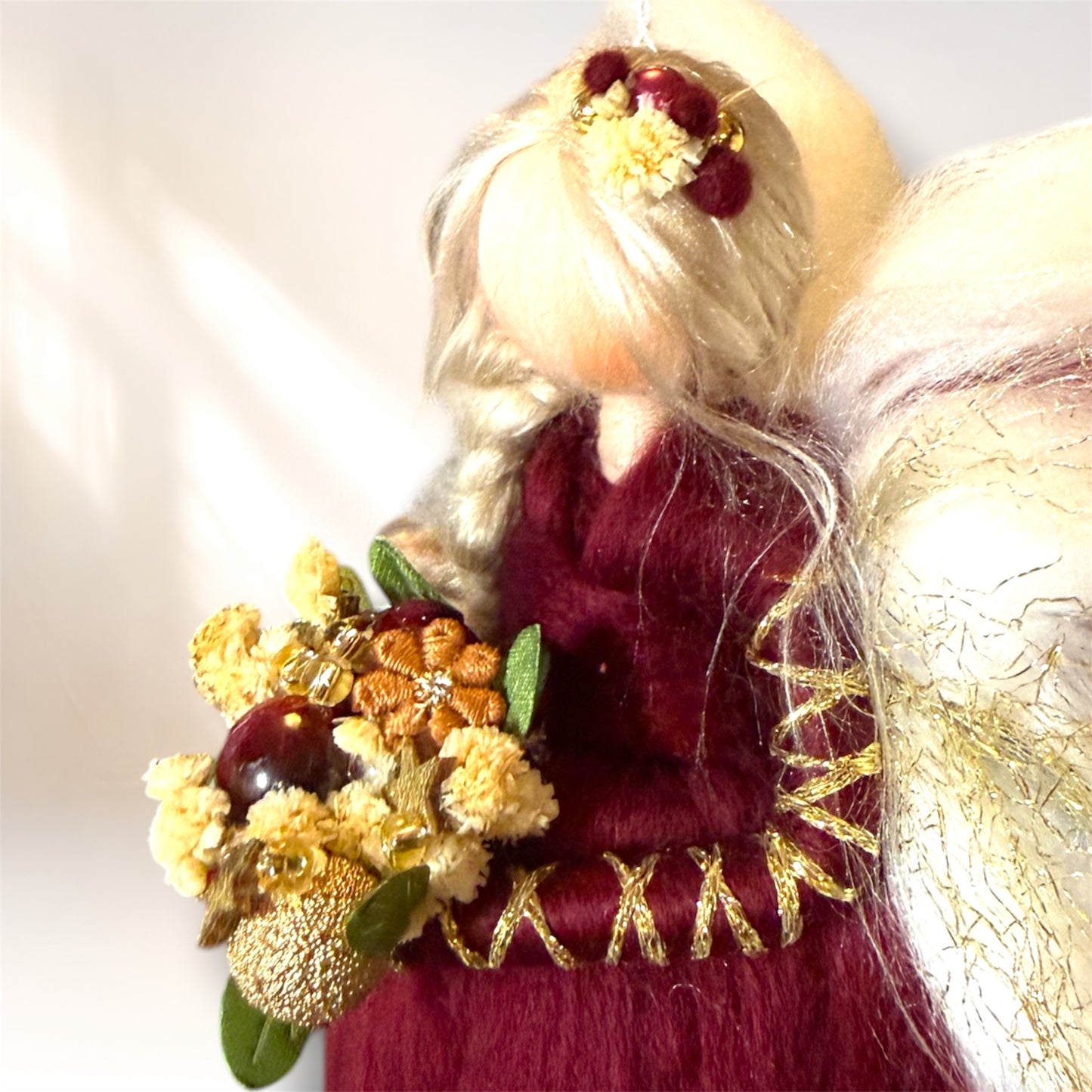 Detalje af uldengel med gyldne detaljer, buket med bær og blomster samt flettet hår